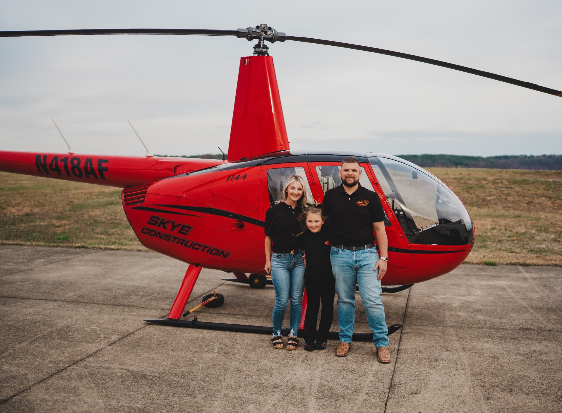 Chelsea Skye, Anistyn Skye and Calib Skye standing in front of the red Skye Construction helicopter